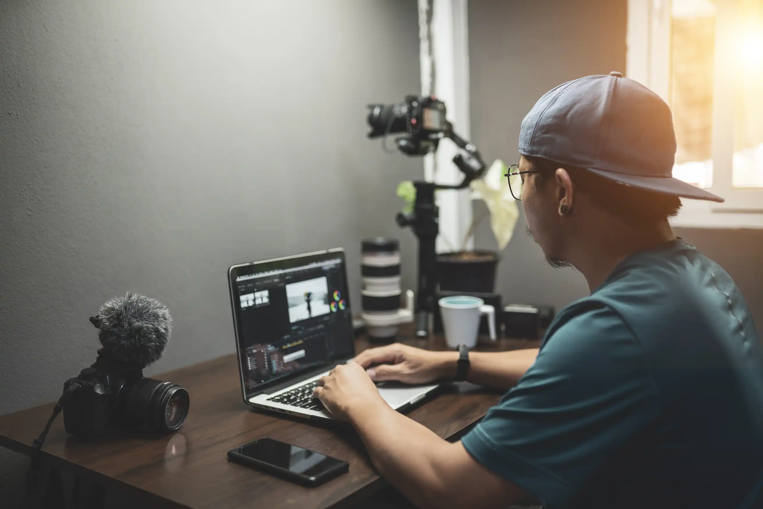 A content creator working on a laptop with camera equipment in the background.